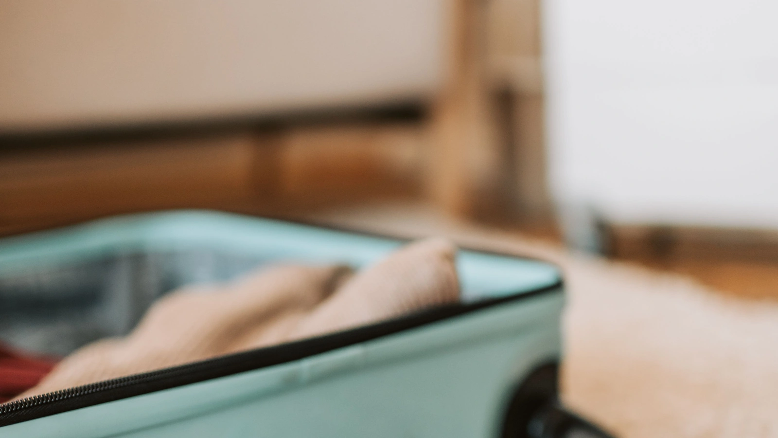 Open suitcase beside travel documents and a toy airplane on a carpet at home.