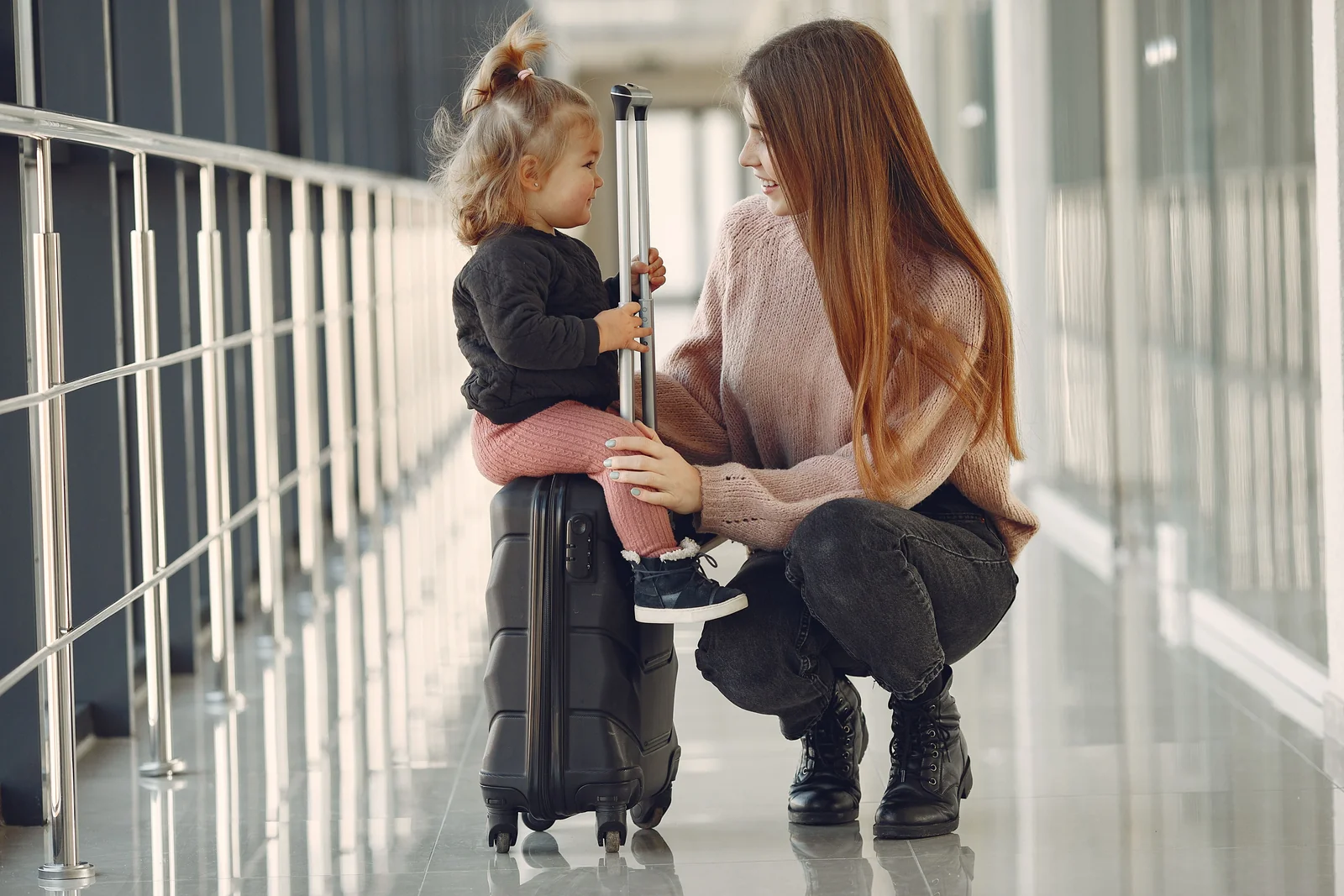 A mother and daughter smiling beside a suitcase at an airport