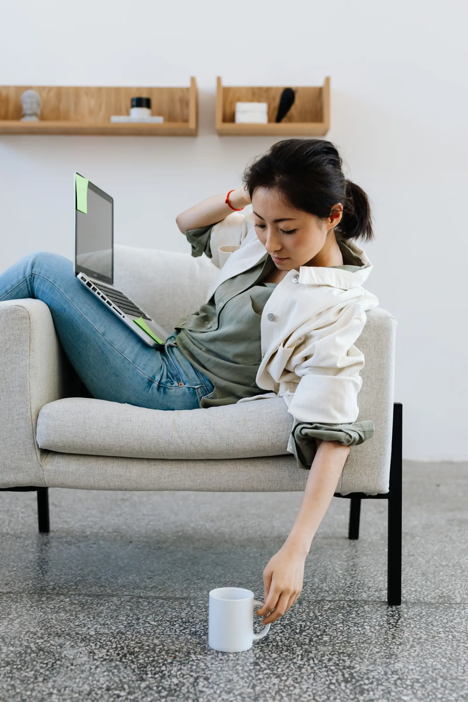 A woman relaxing with a laptop and a cup of coffee beside an armchair