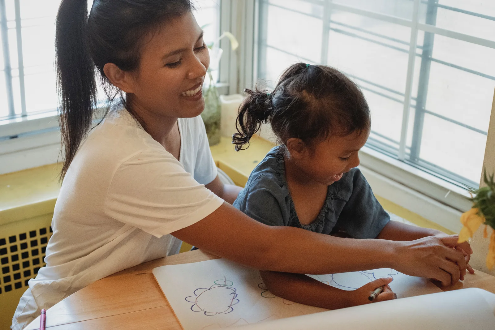 A mother and daughter drawing together at a sunny table