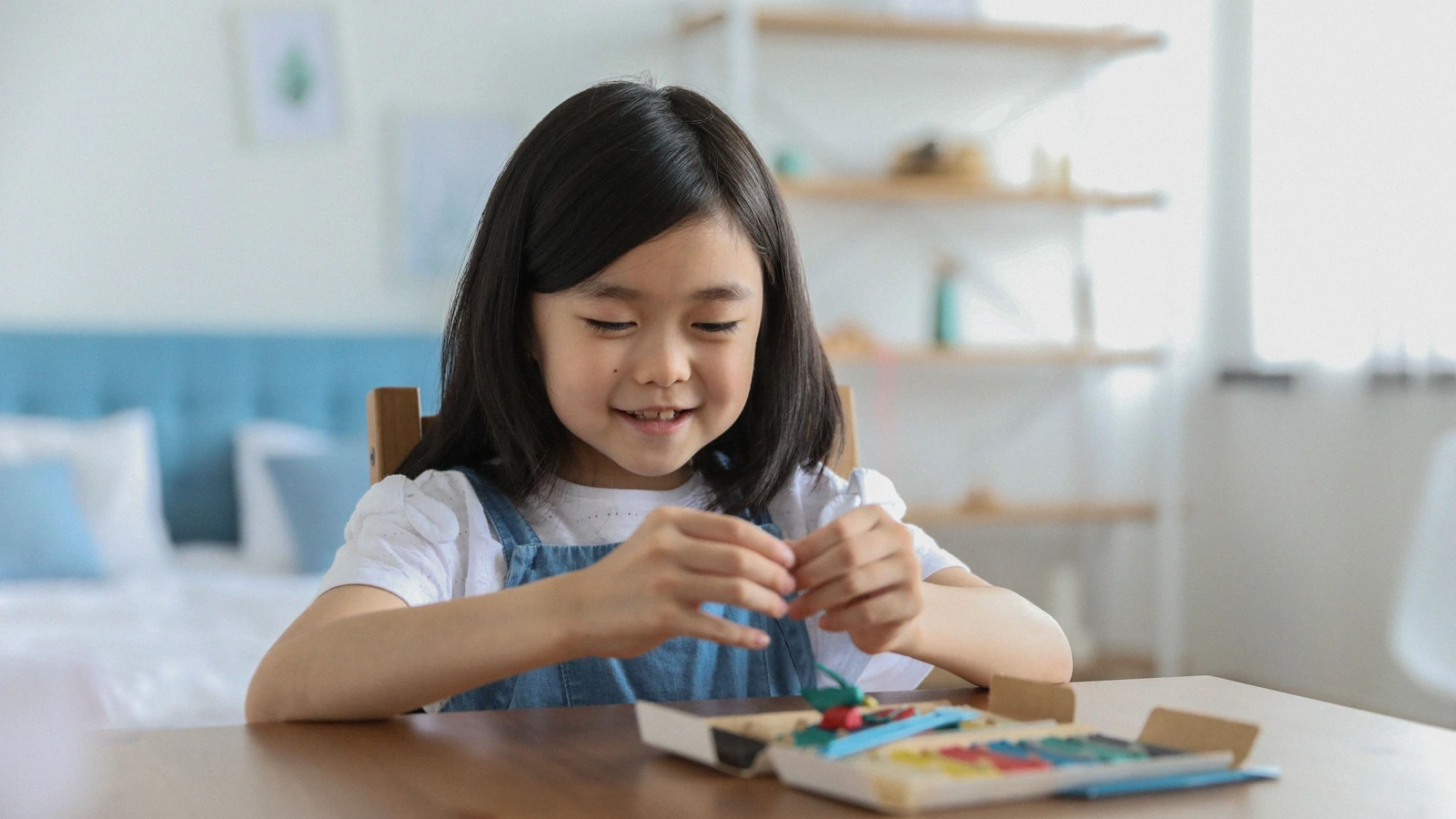 Girl calmly shaping colorful modeling clay at a table at home.