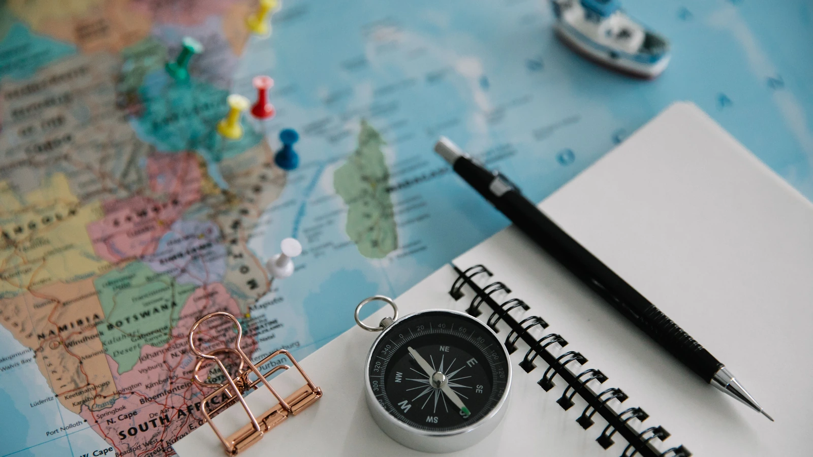 Notebook, pen and compass arranged over a map for travel planning.