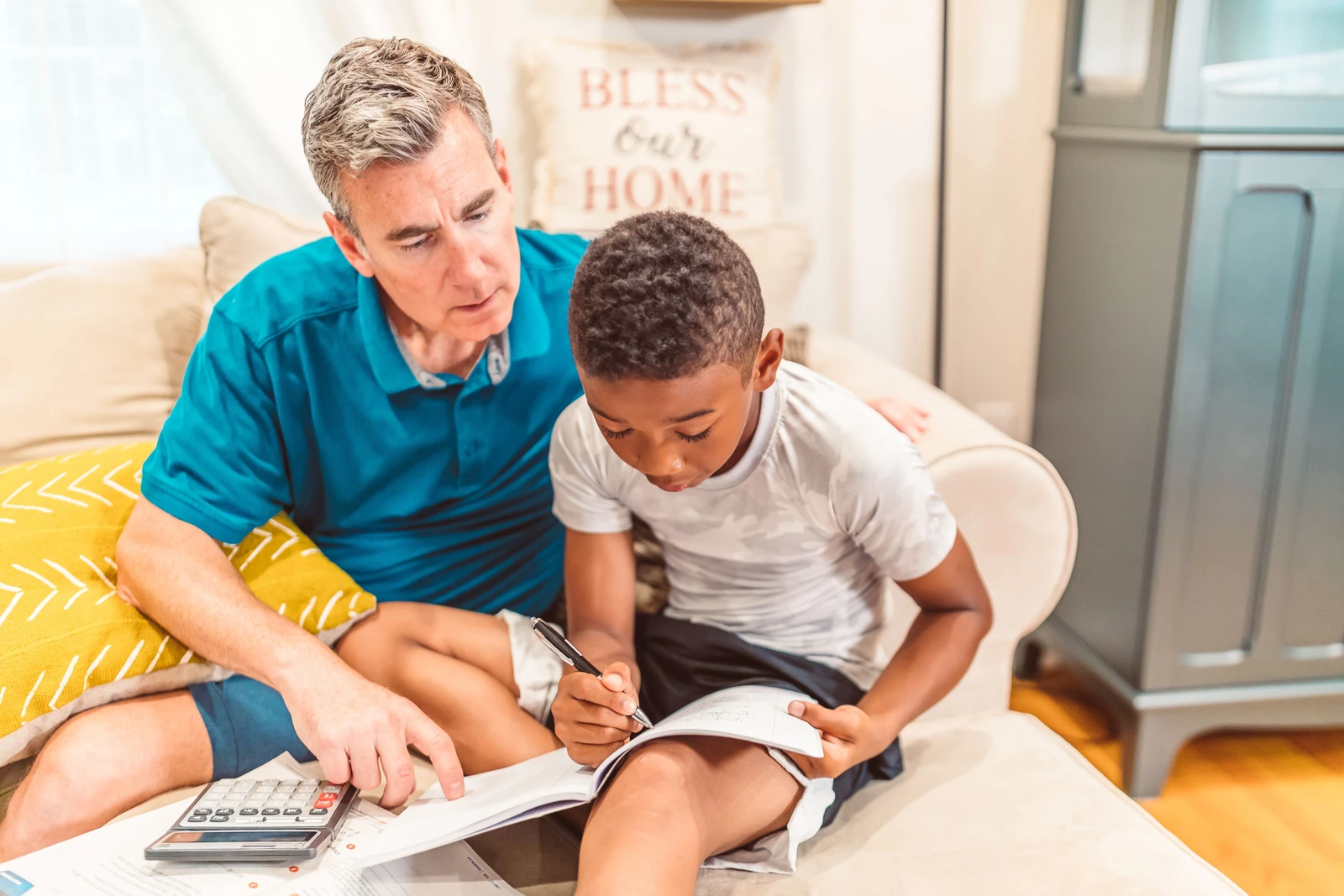 An adult sitting beside a child and helping with a workbook at home
