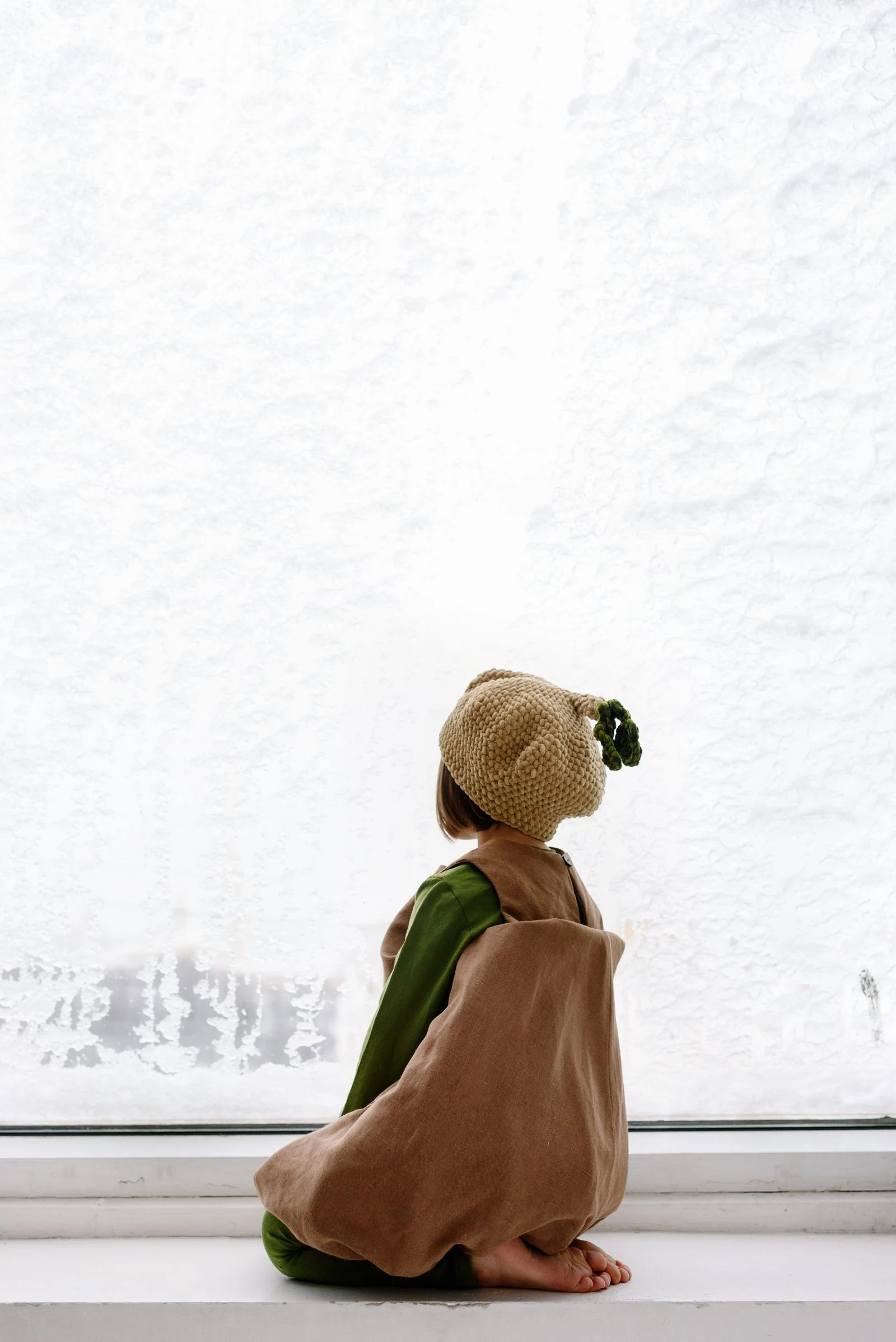 A small child sitting on a window sill, quietly looking outside