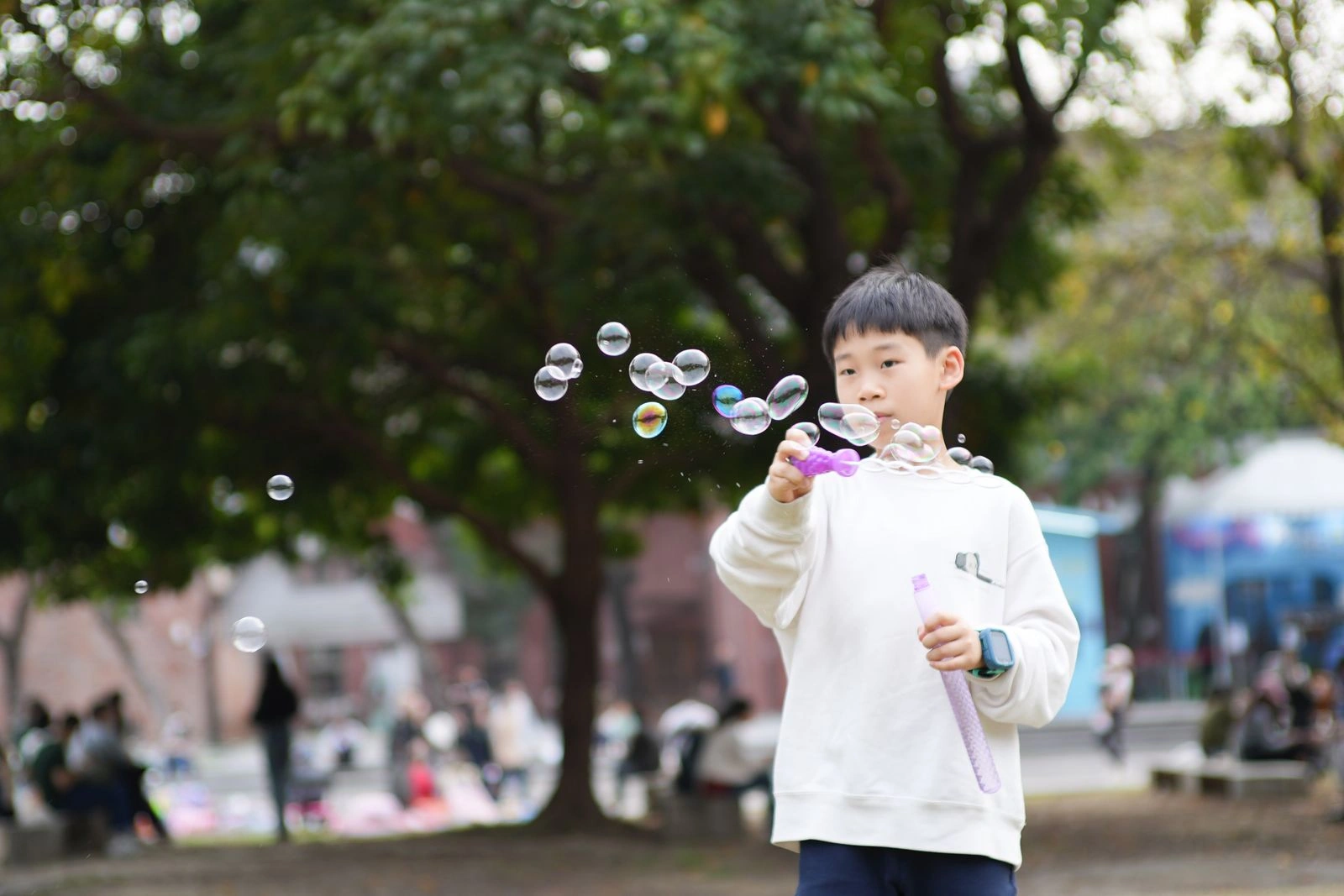 A boy blowing soap bubbles in a leafy park